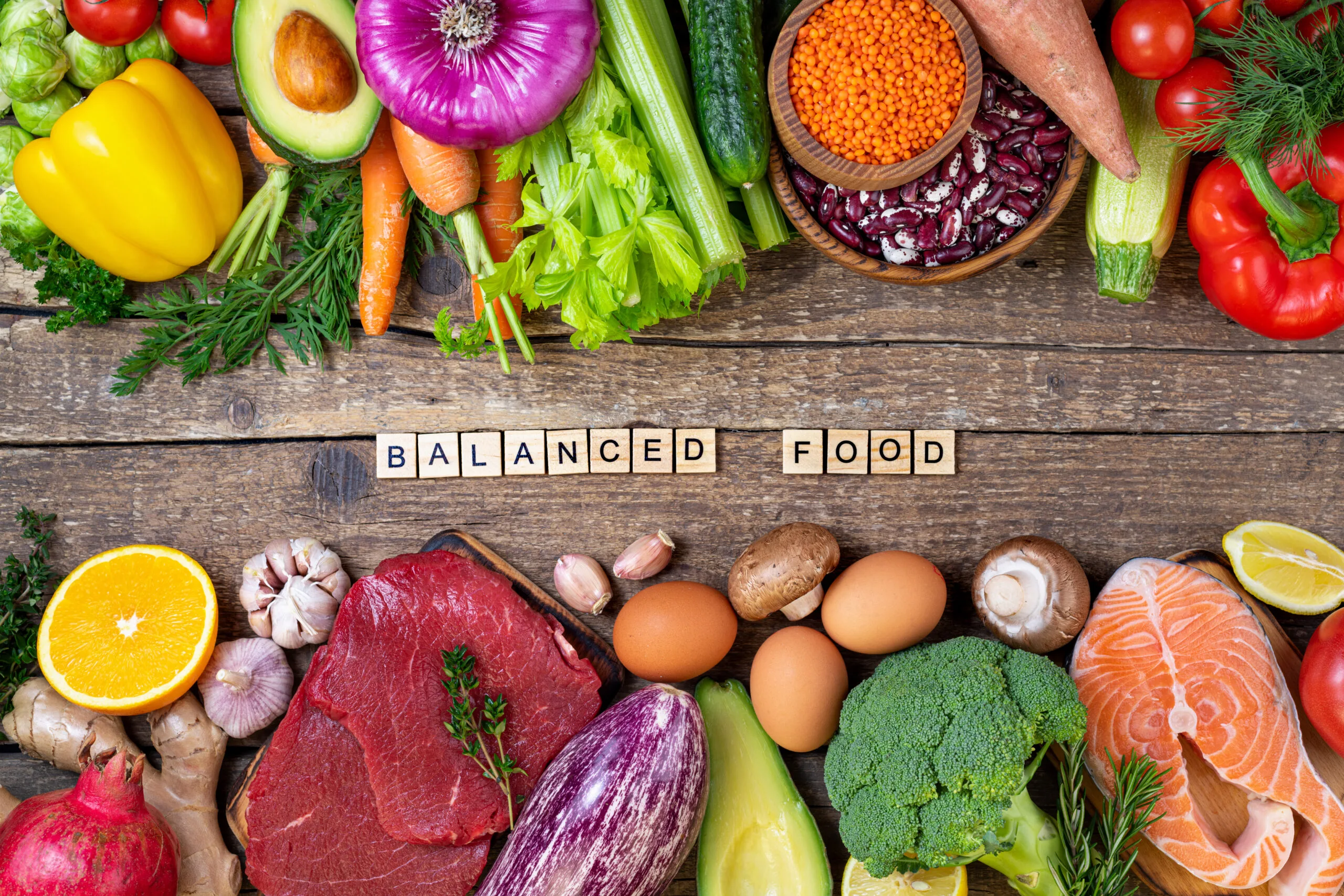 Balanced variety of foods including vegetables, fruits, eggs, fish, and lean meat arranged on a wooden table.