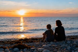 A caring parent and child sitting together on a beach at sunset, symbolizing the love, hope, and gentle concern that often lead families to explore growth hormone therapy for healthy children.