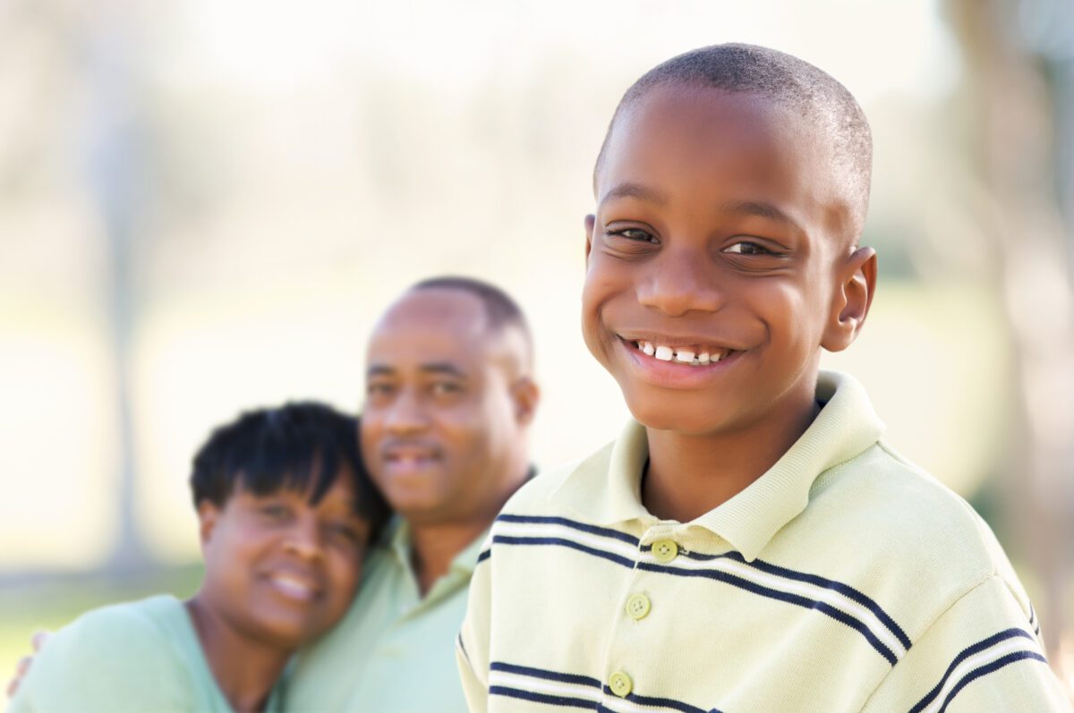 A young boy smiling confidently with his parents in the background, representing a family exploring growth hormone therapy options at I Grow Clinic for children with idiopathic short stature.