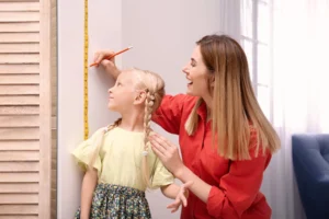 A parent measuring their child's height at home against a wall chart, tracking monthly growth velocity to monitor the progress of the growth spurt.