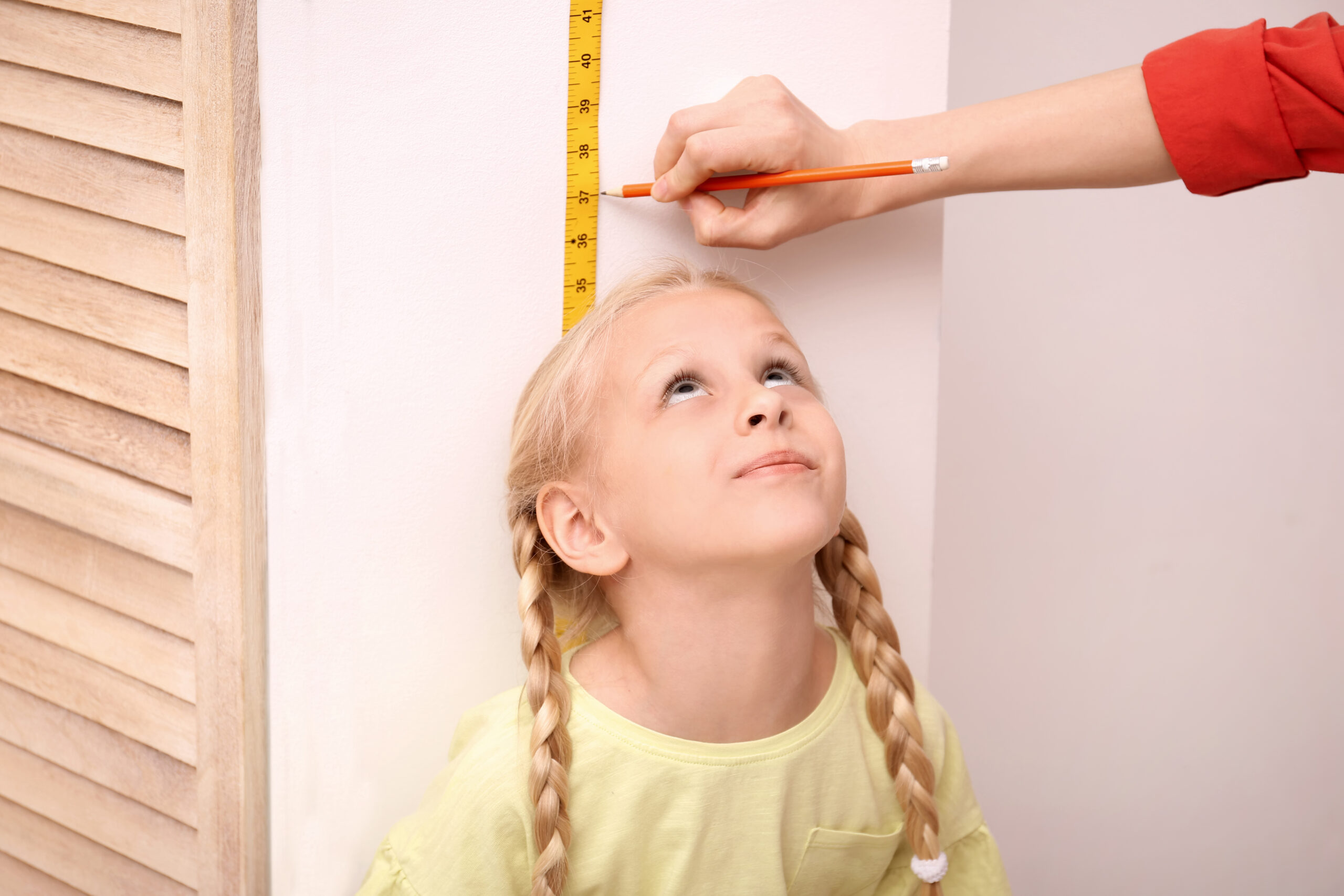 Parent measuring child height at home tracking slow growth before visiting a pediatric growth clinic