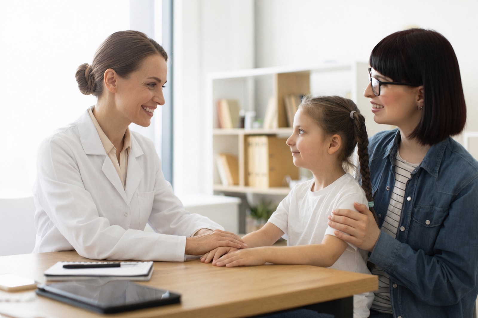 Warm pediatric growth specialist smiling with a young girl and her mother during a growth consultation