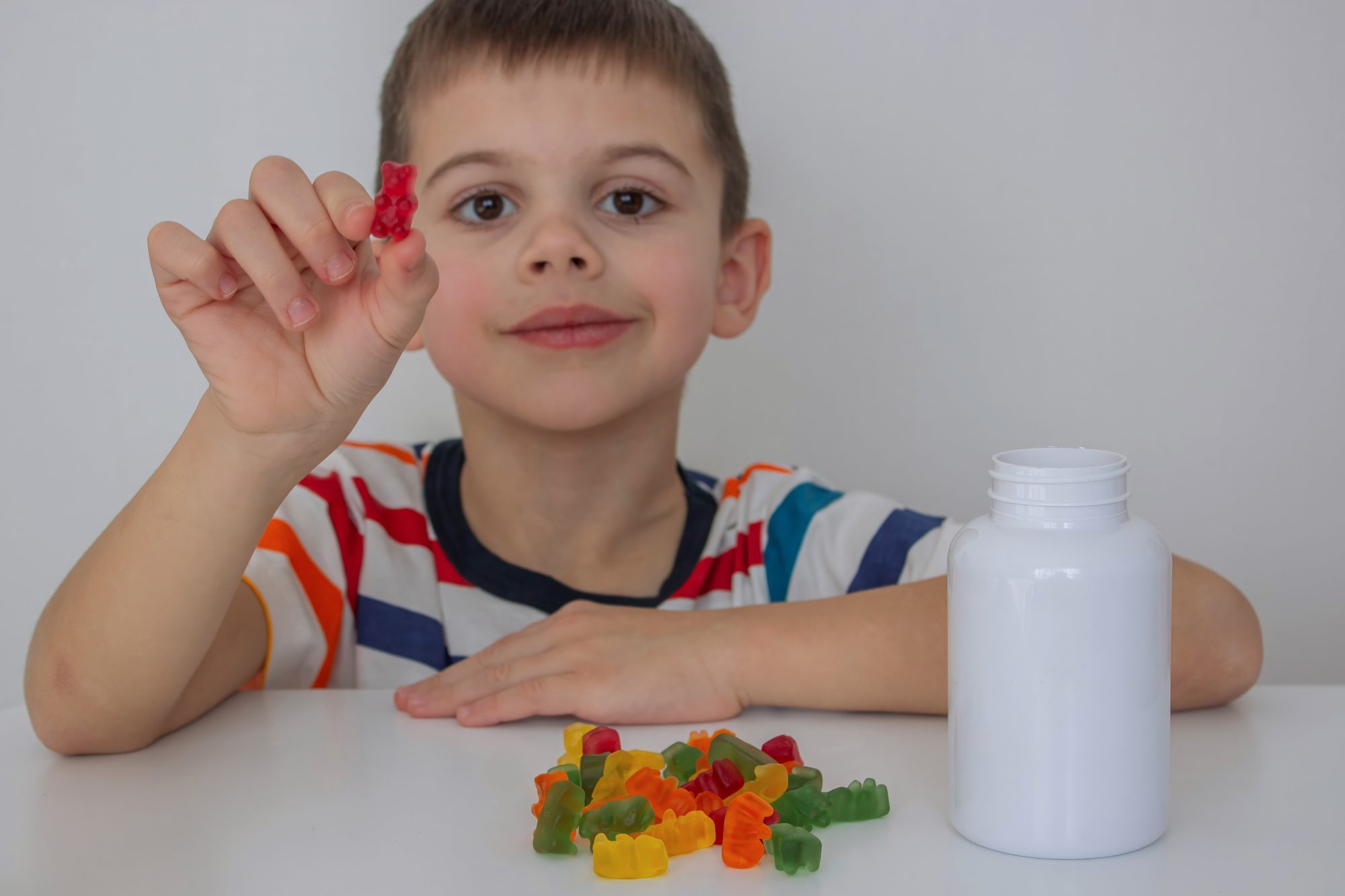 Young boy holding up a gummy vitamin next to a supplement bottle, asking if height gummies work