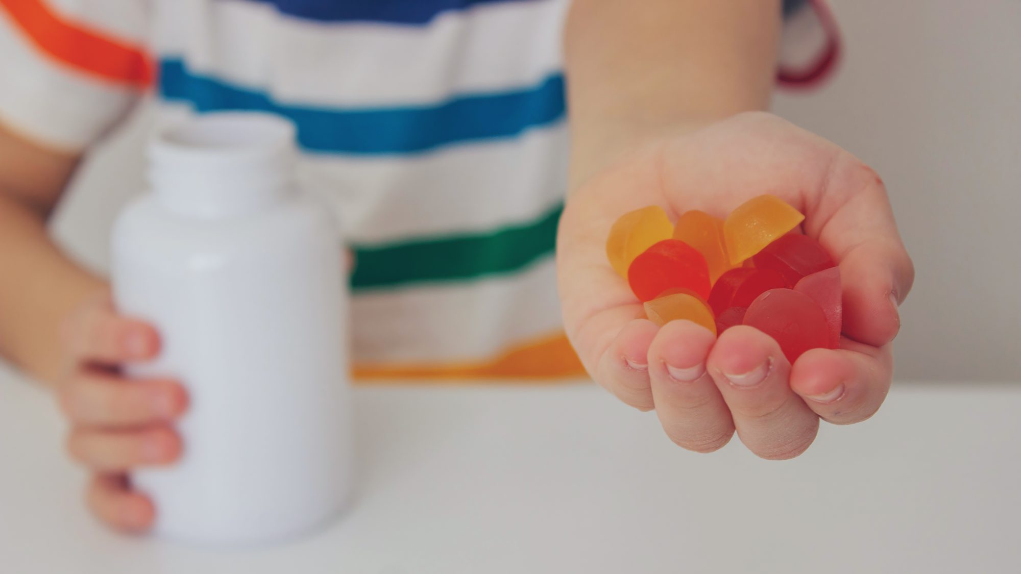 Child holding a handful of gummy vitamins beside a supplement bottle, a common height supplement for kids