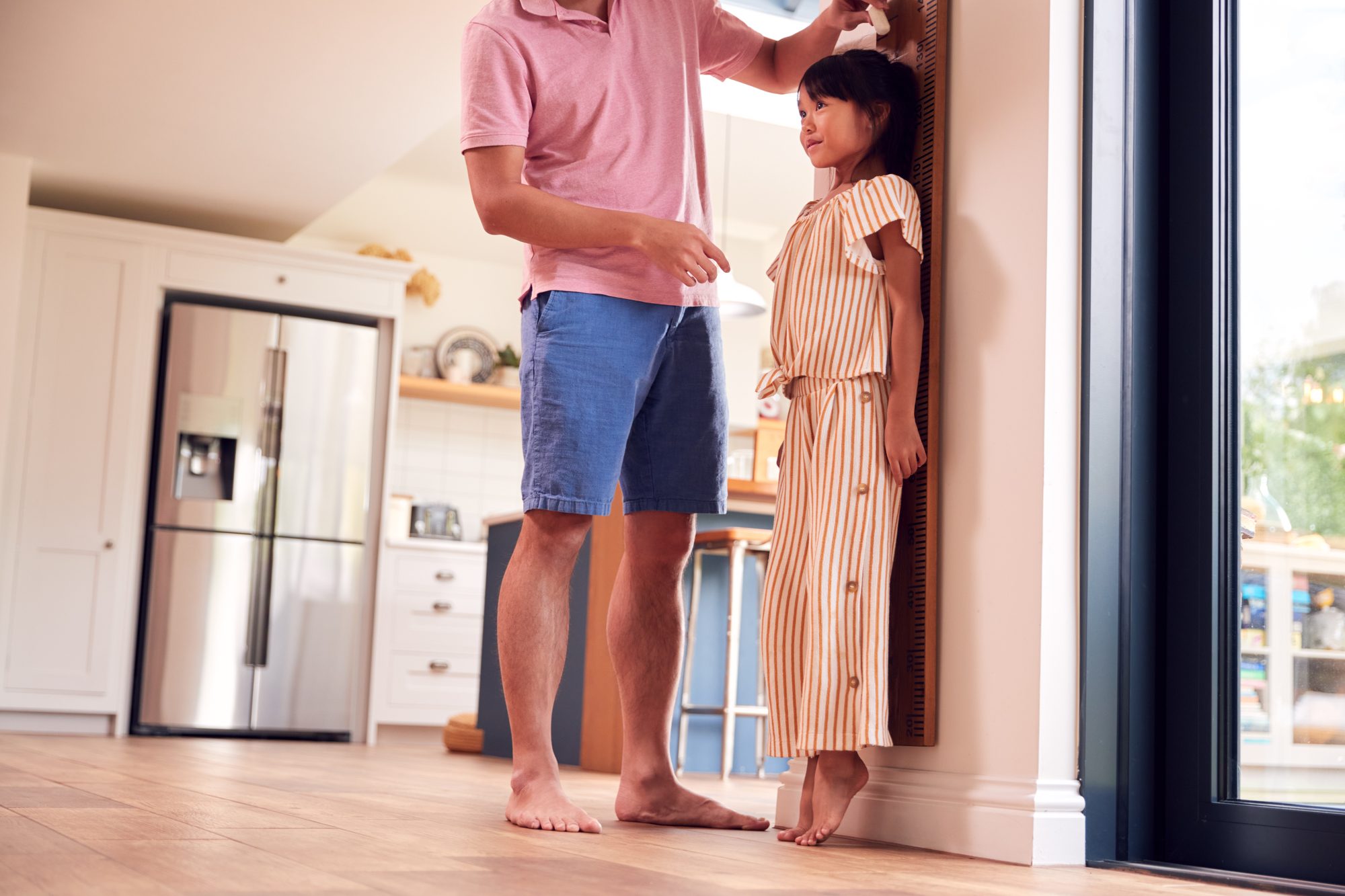 Parent measuring a child's height at home to track growth velocity over time